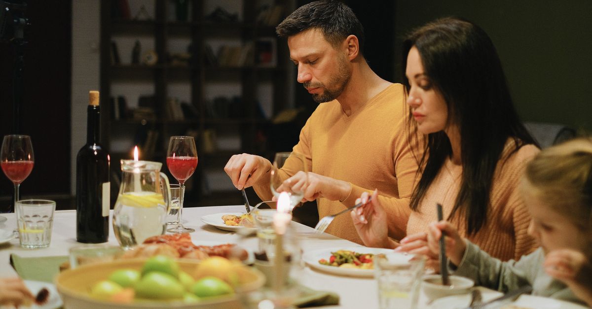 A family gathered around a dinner table indoors, enjoying a meal together with wine and candles.
